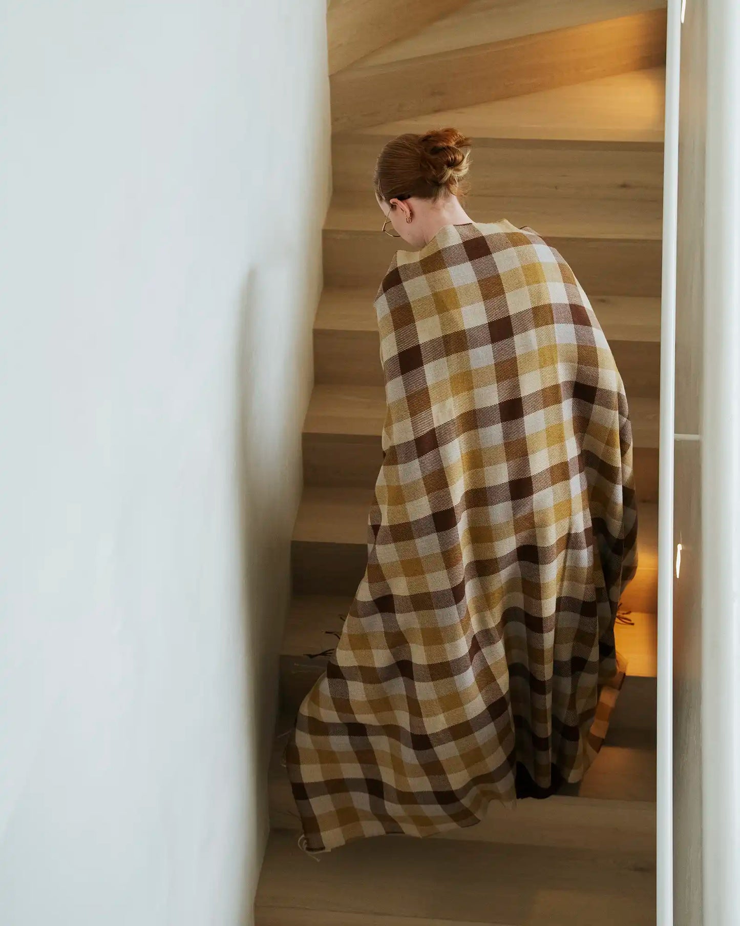 Person wrapped in a plaid blanket descending a staircase