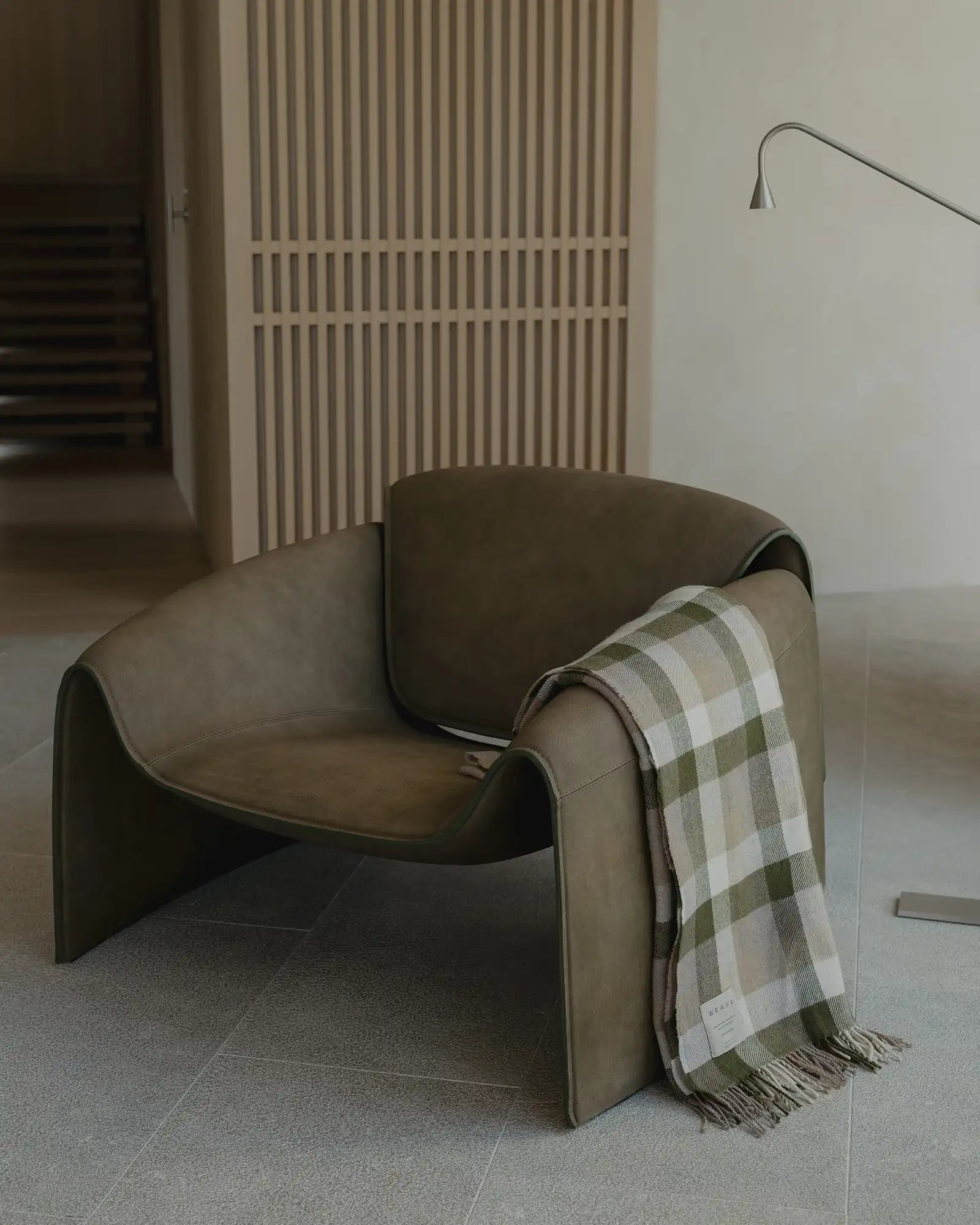 Brown armchair with a plaid blanket draped over it in a minimalistic room.