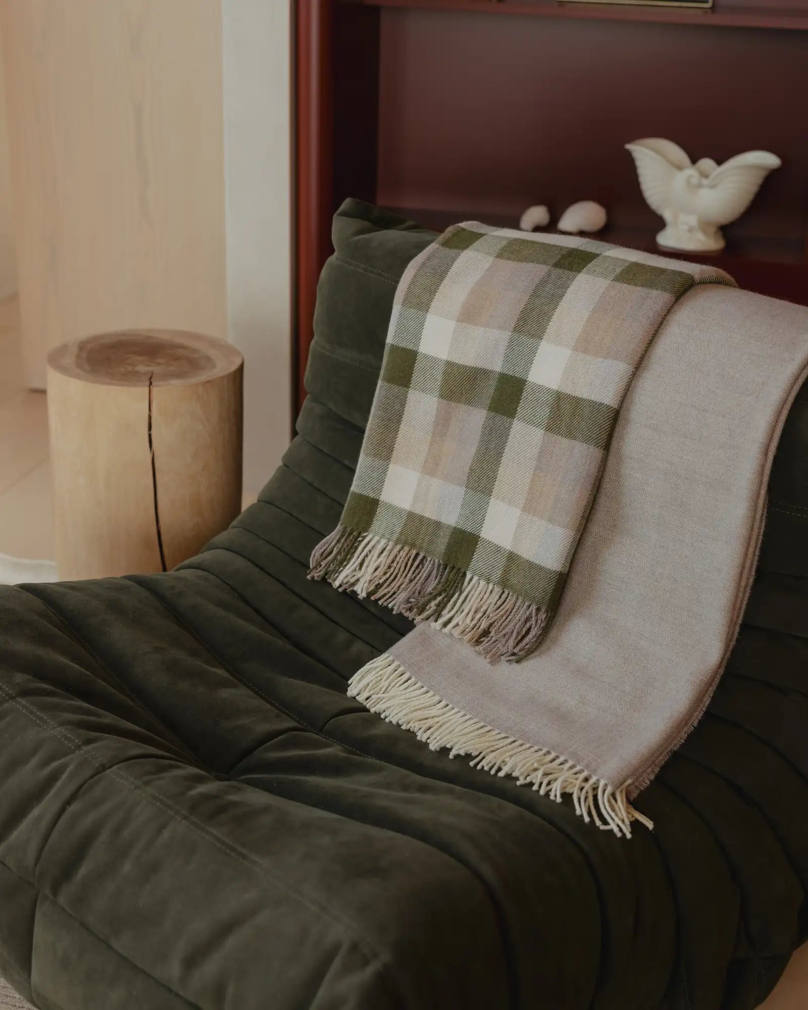 Green plaid blanket draped over a green armchair with a wooden side table and decorative items in the background.