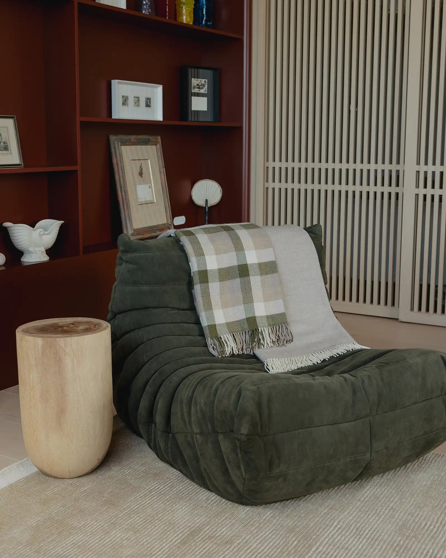 Green bean bag chair with a plaid blanket in a room with a bookshelf and decorative items.