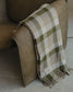 Plaid blanket draped over a brown armchair on a tiled floor.