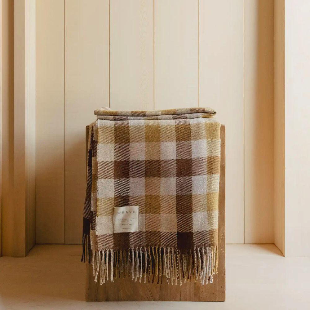 Plaid blanket with fringes draped over a wooden surface against a striped wall.