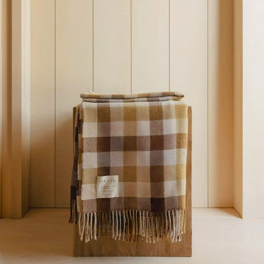 Plaid blanket with fringes draped over a wooden surface against a striped wall.