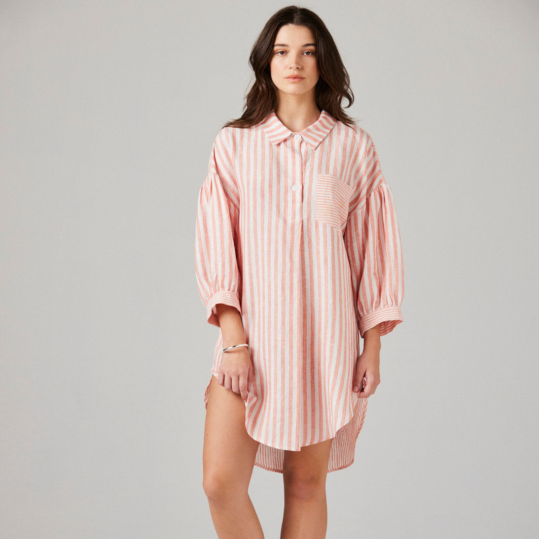Woman wearing a pink striped nightshirt on a plain background