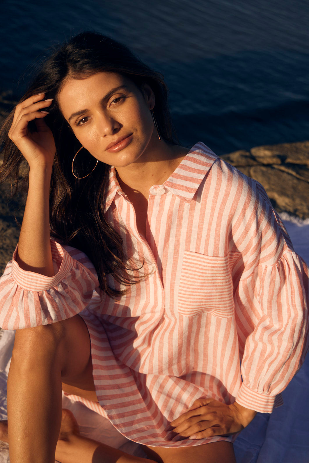 Woman in a pink and white striped shirt sitting by a body of water.