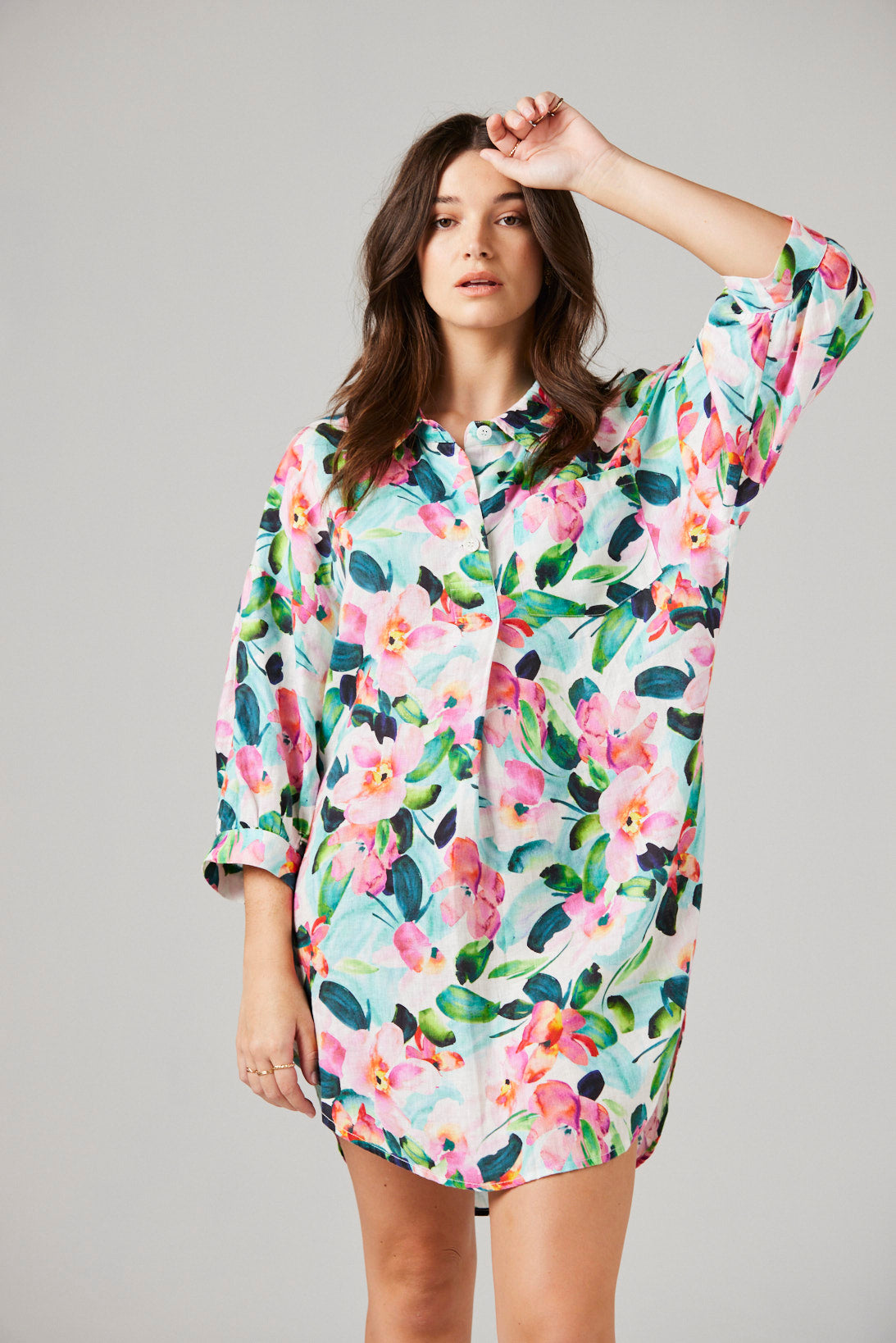 Woman wearing a colorful floral shirt dress against a plain background