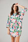 Woman wearing a colorful floral shirt dress against a plain background