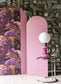 Pink lamp with white bulb on a small round table against a textured wall.
