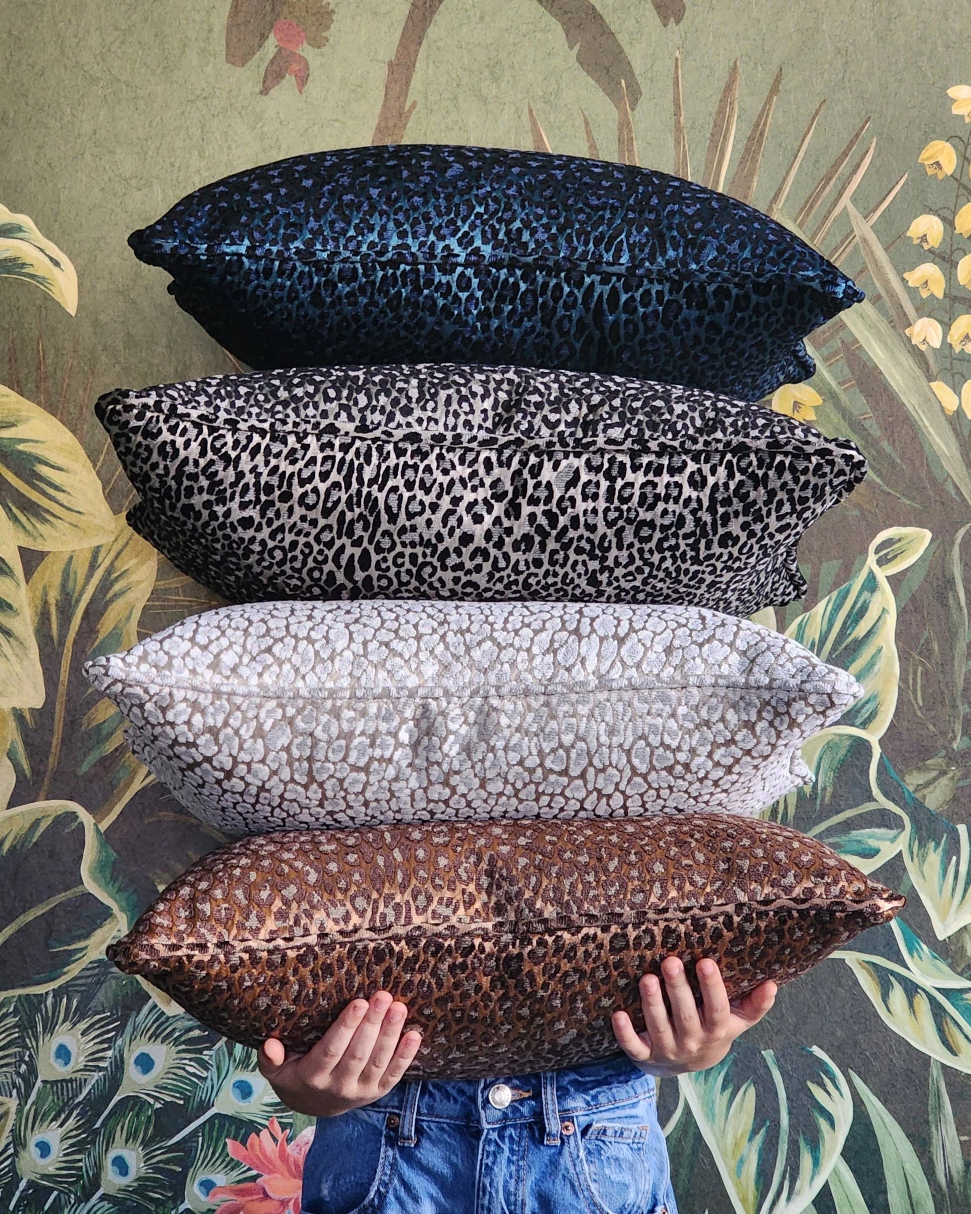 Four patterned pillows stacked with a person holding the bottom one against a decorative background.