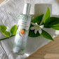 Room spray bottle with green leaves and white flower on a white cloth