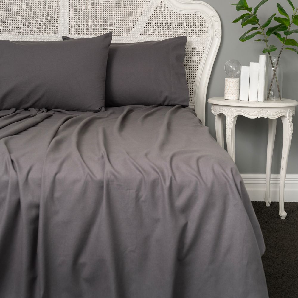 Gray bedding set on a bed with a white headboard and side table in a room.