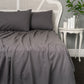 Gray bedding set on a bed with a white headboard and side table in a room.