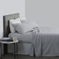 A neatly made bed with a striped duvet cover in a neutral color, accompanied by matching pillows and a small table with a book and a cup beside the bed.