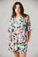 Woman wearing a colorful floral pajama set against a plain background