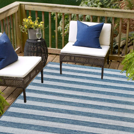 Outdoor seating area with striped rug, wicker chairs, and blue cushions on a wooden deck.