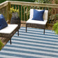Outdoor seating area with striped rug, wicker chairs, and blue cushions on a wooden deck.