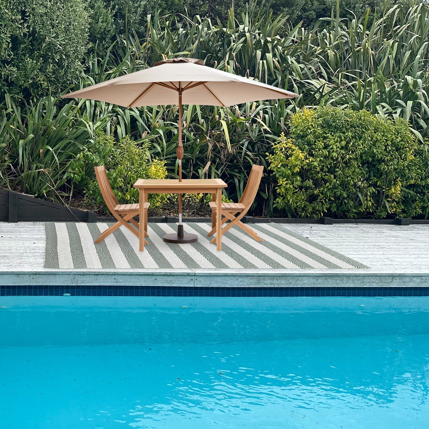 Outdoor setting with a table, chairs, and umbrella by a poolside.