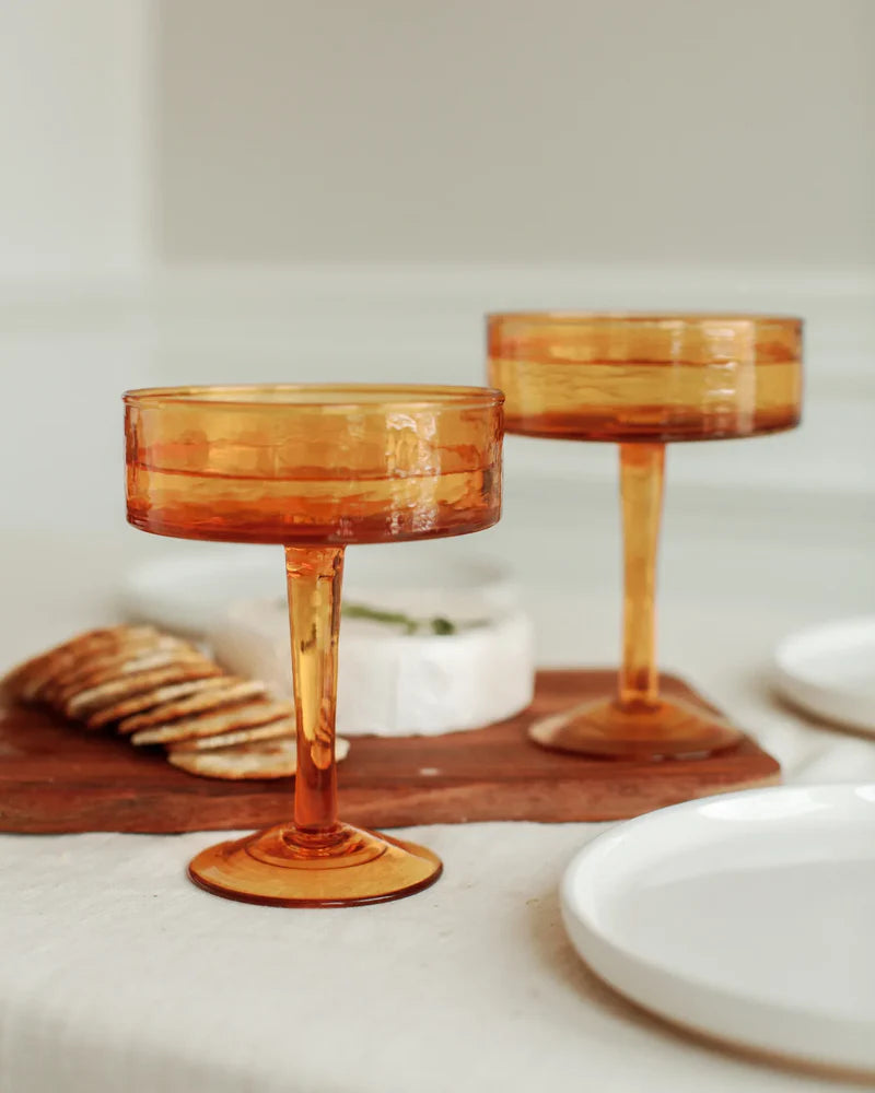 Two amber-colored cocktail glasses on a table with a neutral background