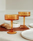 Two amber-colored cocktail glasses on a table with a neutral background