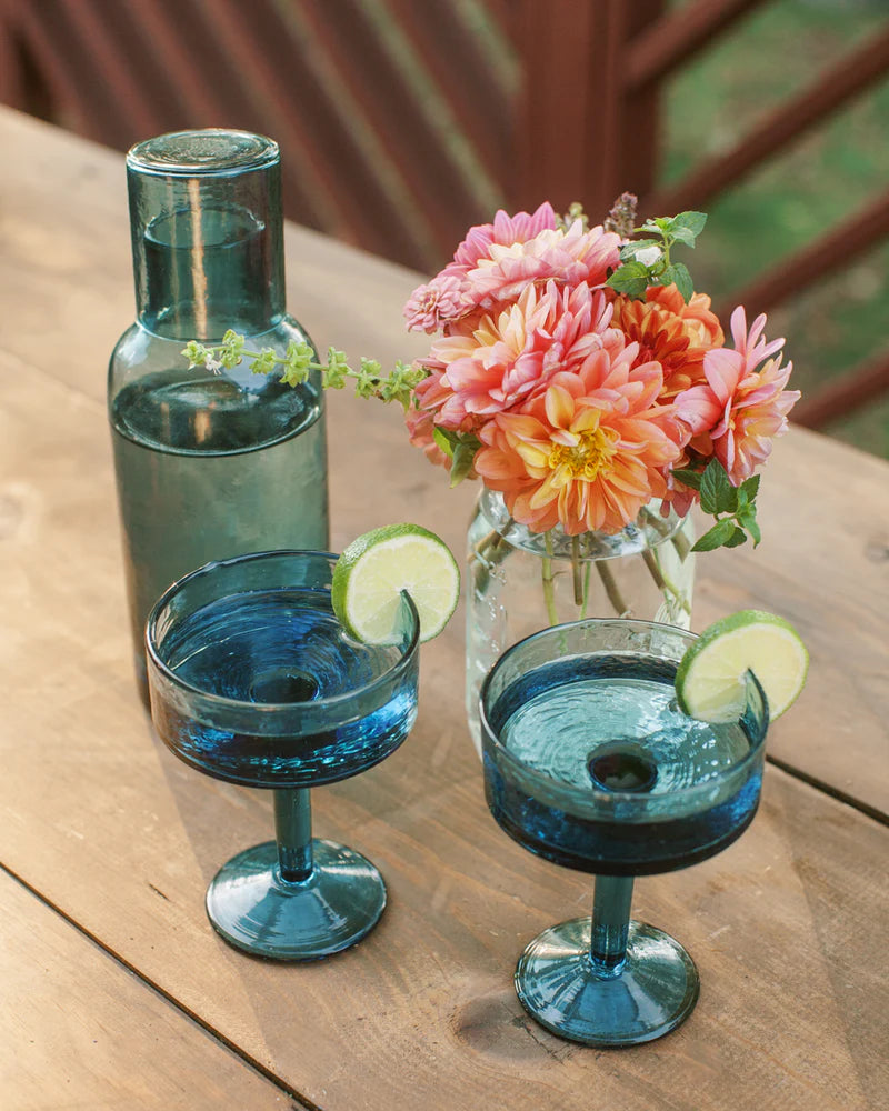 Two blue cocktail glasses with lime wedges and flowers on a wooden table