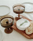 Wooden cutting board with cheese, crackers, and glasses on a white surface