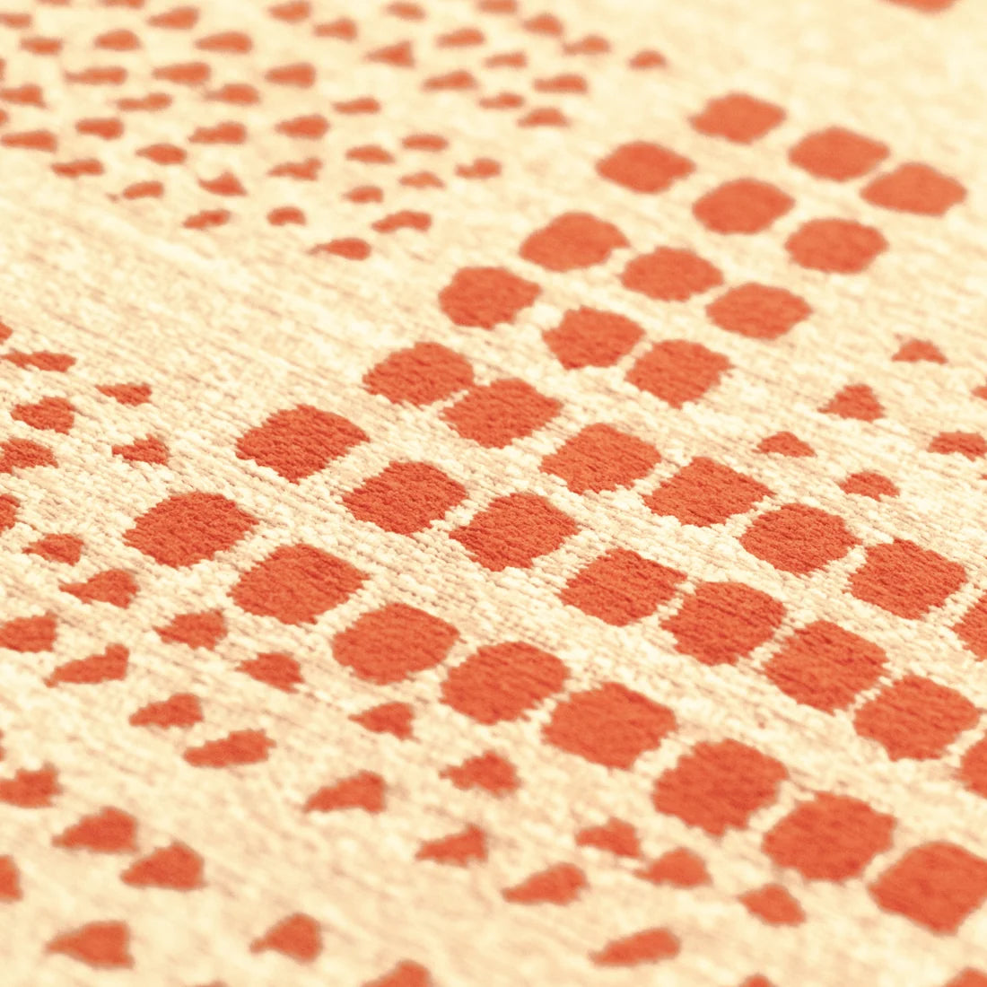 Close-up of a woven textile with a repeating geometric pattern of orange-red squares and dots on a warm beige background.
