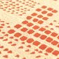 Close-up of a woven textile with a repeating geometric pattern of orange-red squares and dots on a warm beige background.