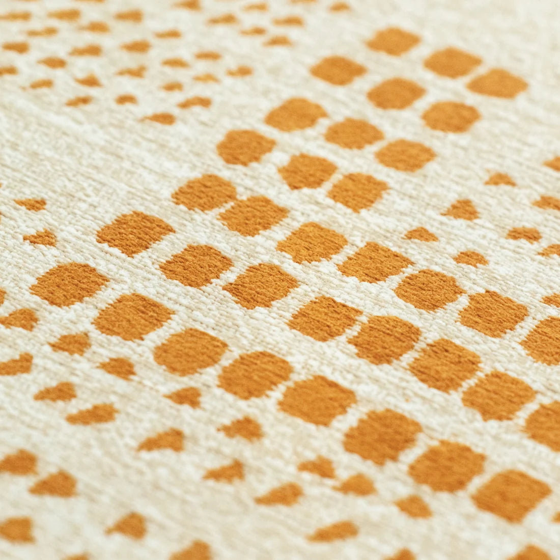 Close-up of a textured cream fabric with a repeating pattern of small orange squares and dots.