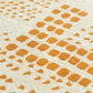Close-up of a textured cream fabric with a repeating pattern of small orange squares and dots.