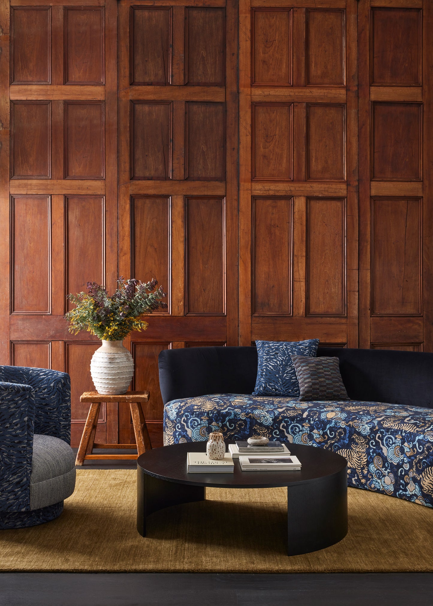 Modern living room with wooden paneled wall, blue sofa, and round coffee table.