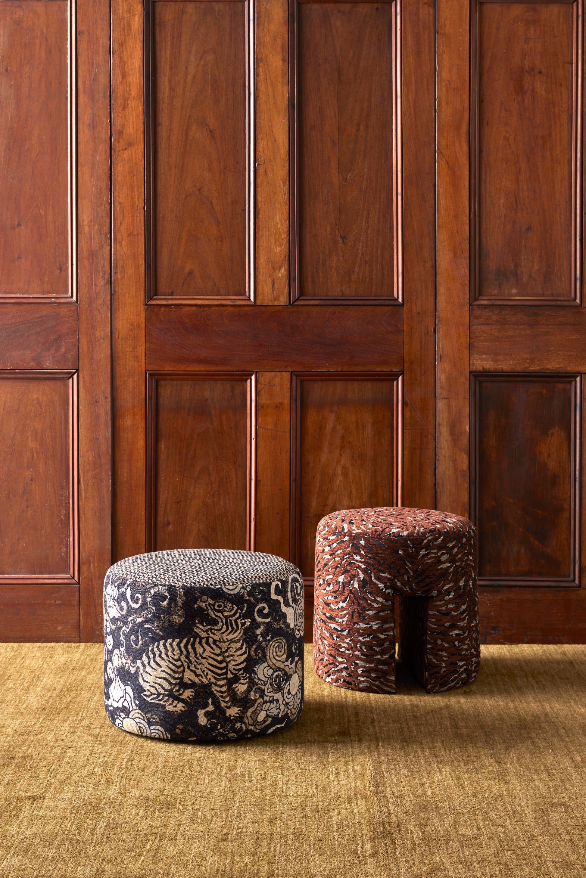 Two patterned stools against a wooden paneled wall.