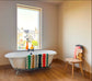 White freestanding bathtub with a colorful towel next to a window in a room with wooden flooring.