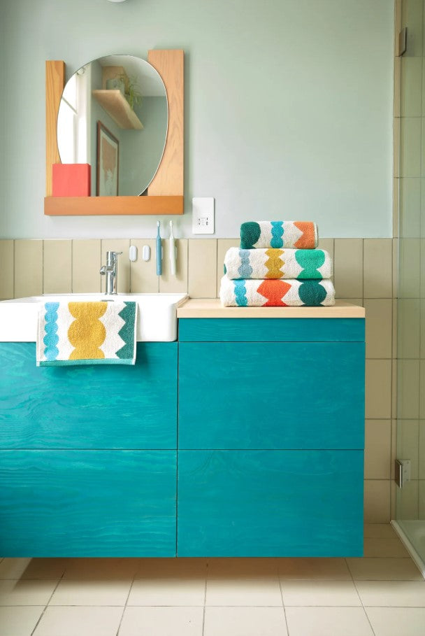 Bathroom with teal vanity, colorful towels, and a mirror.