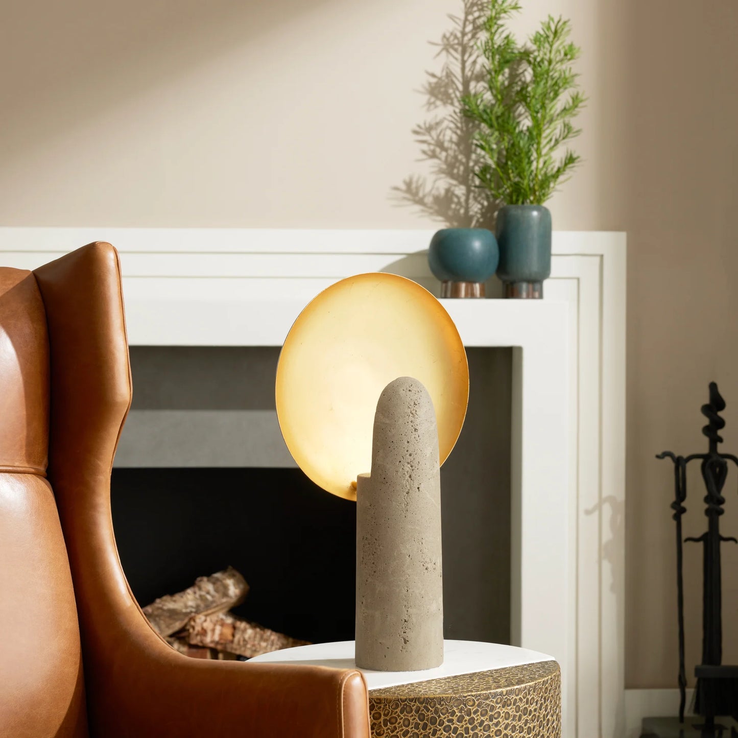 Cylindrical table lamp with a textured base on a side table next to a brown armchair.