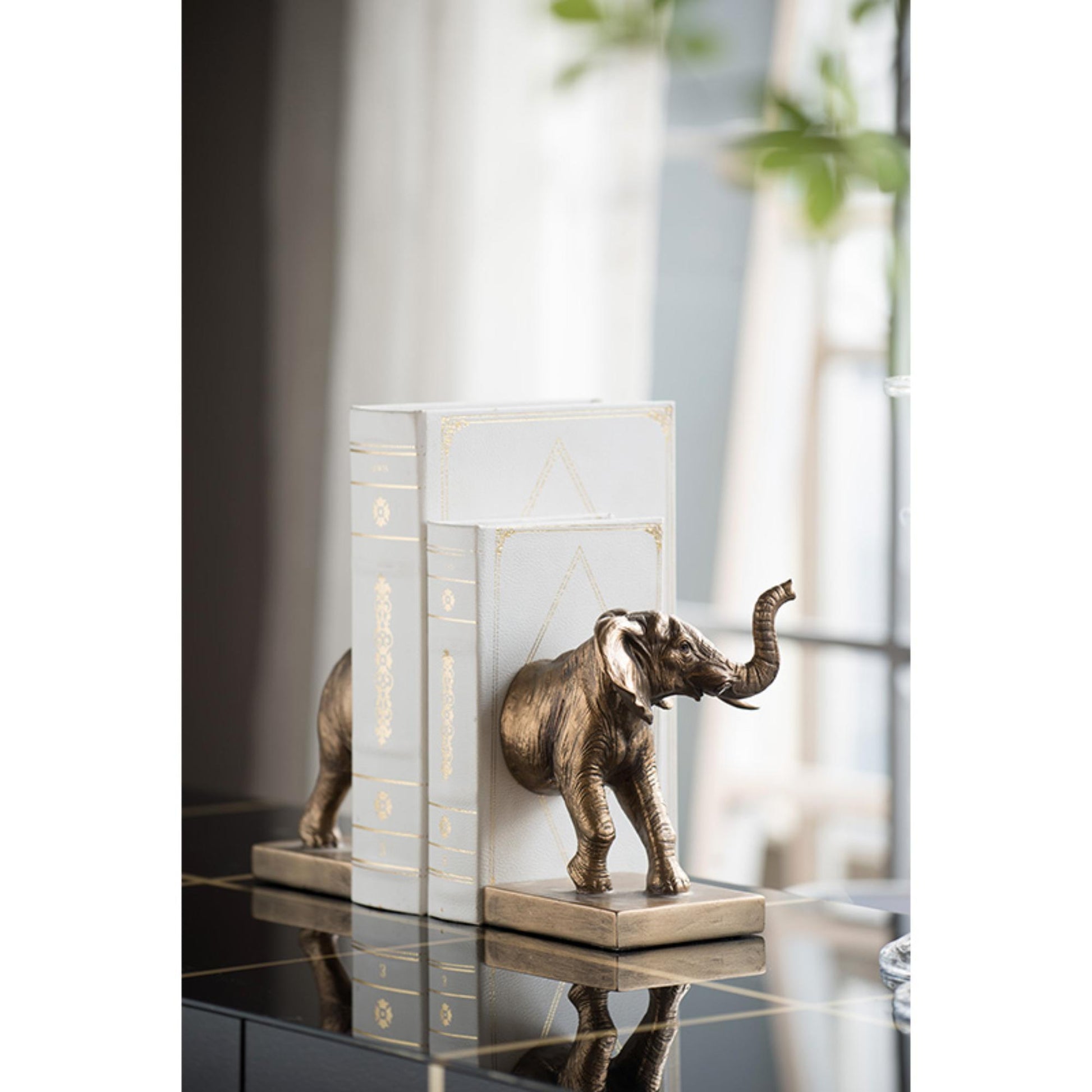 Decorative elephant bookends on a reflective surface with a blurred background