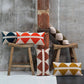oblong cushions with rhombus patterns in courdurouy standing against a wooden pole and also on wooden stool
