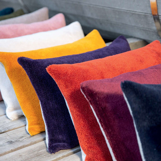 Row of brightly coloured velvet cushions leaning up against each other in blue, purple, paprika, burgundy, ochre, white and pink