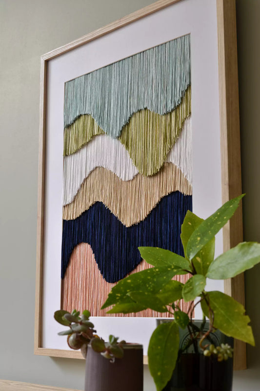 Framed abstract wall art with wavy color patterns on a light green wall.