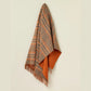 Plaid blanket with orange and brown colors draped over a light beige background