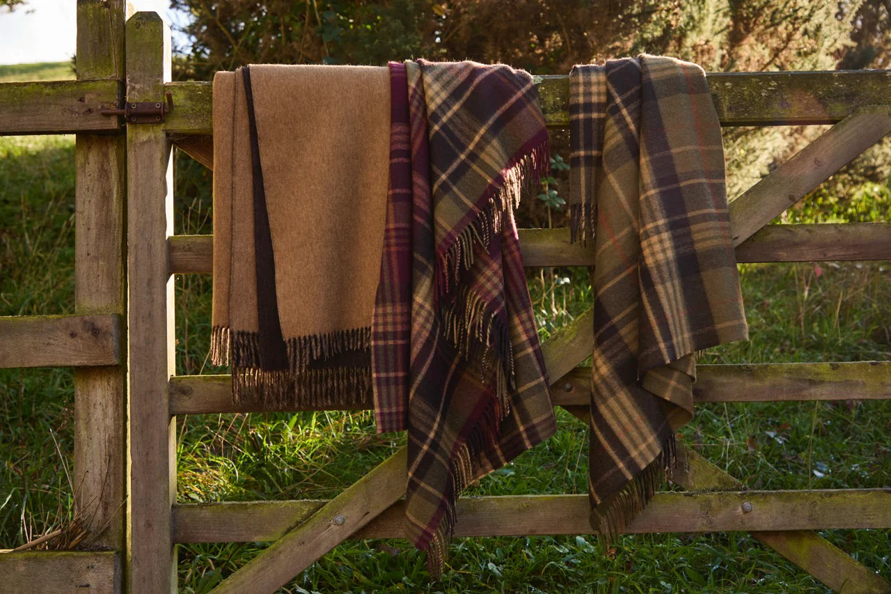 Three plaid blankets draped over a wooden fence with a natural background