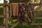 Three plaid blankets draped over a wooden fence with a natural background