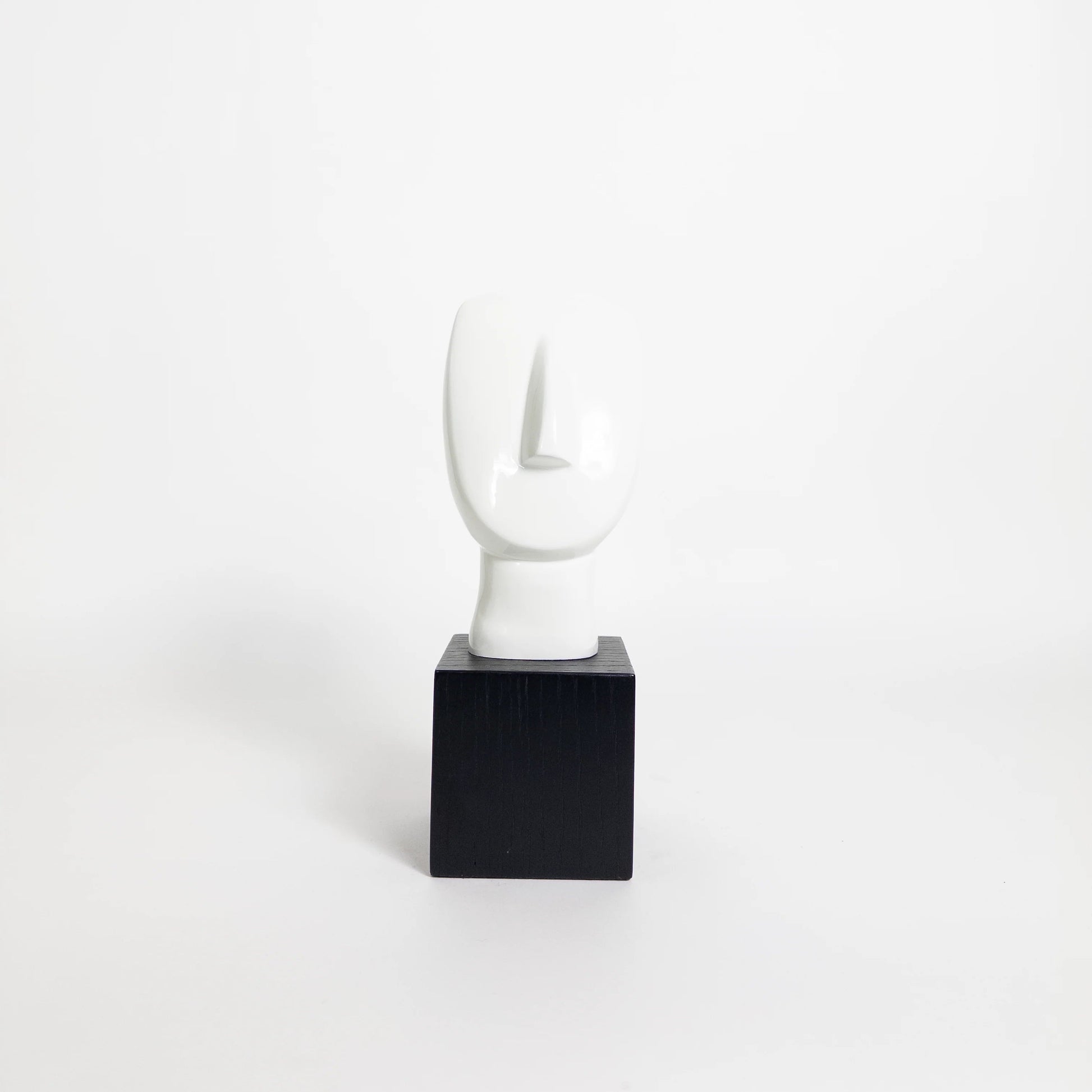 A minimalist abstract white sculpture on a black square pedestal, photographed against a seamless white studio background.