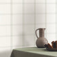 Gray ceramic pitcher on a table with a plaid wallpaper background