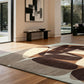 abstract rug with organic shapes in brown, beige and cream on a wooden floor with black modern furniture and art