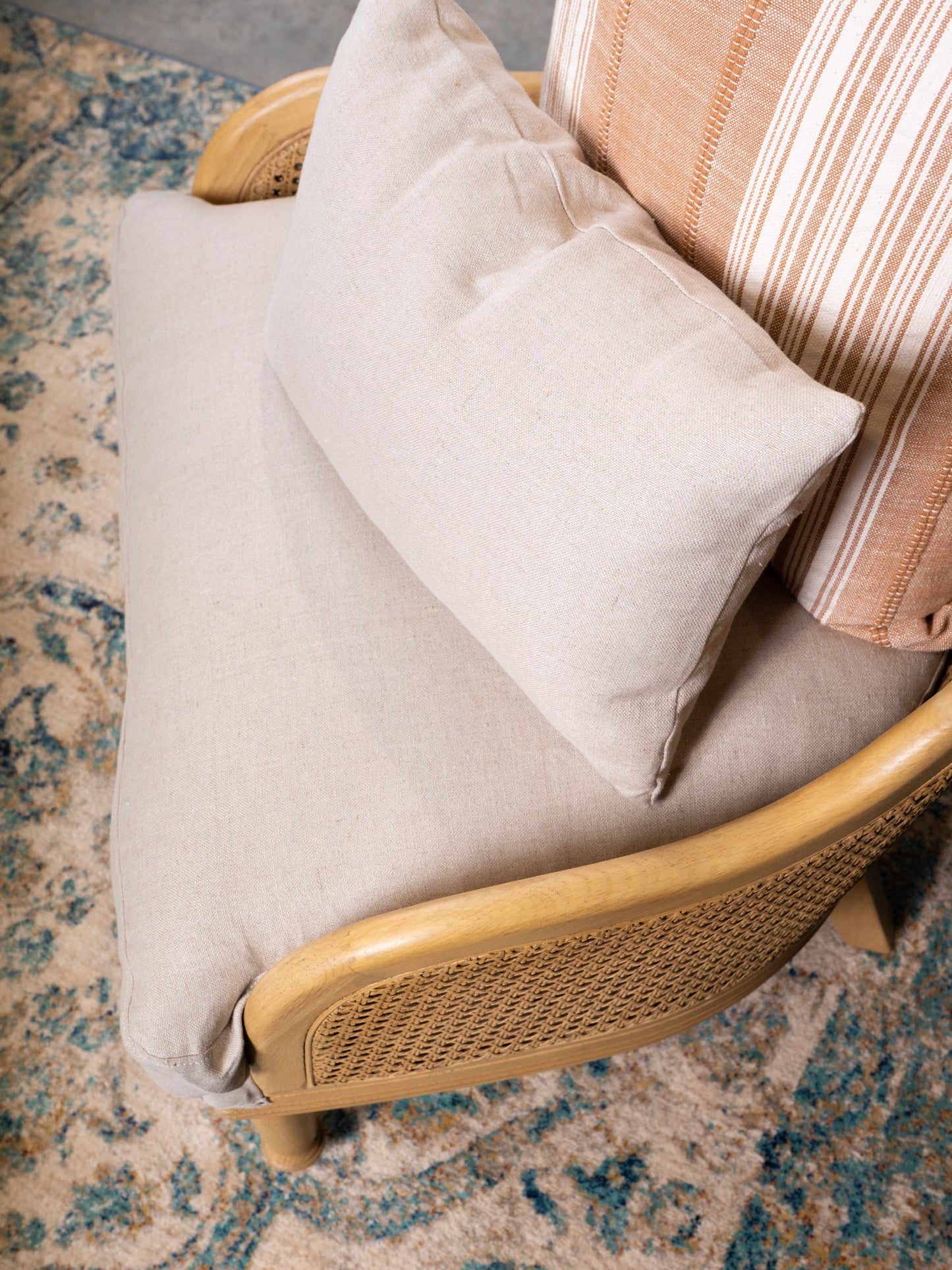 Wicker chair with beige cushion and striped pillow on a textured rug