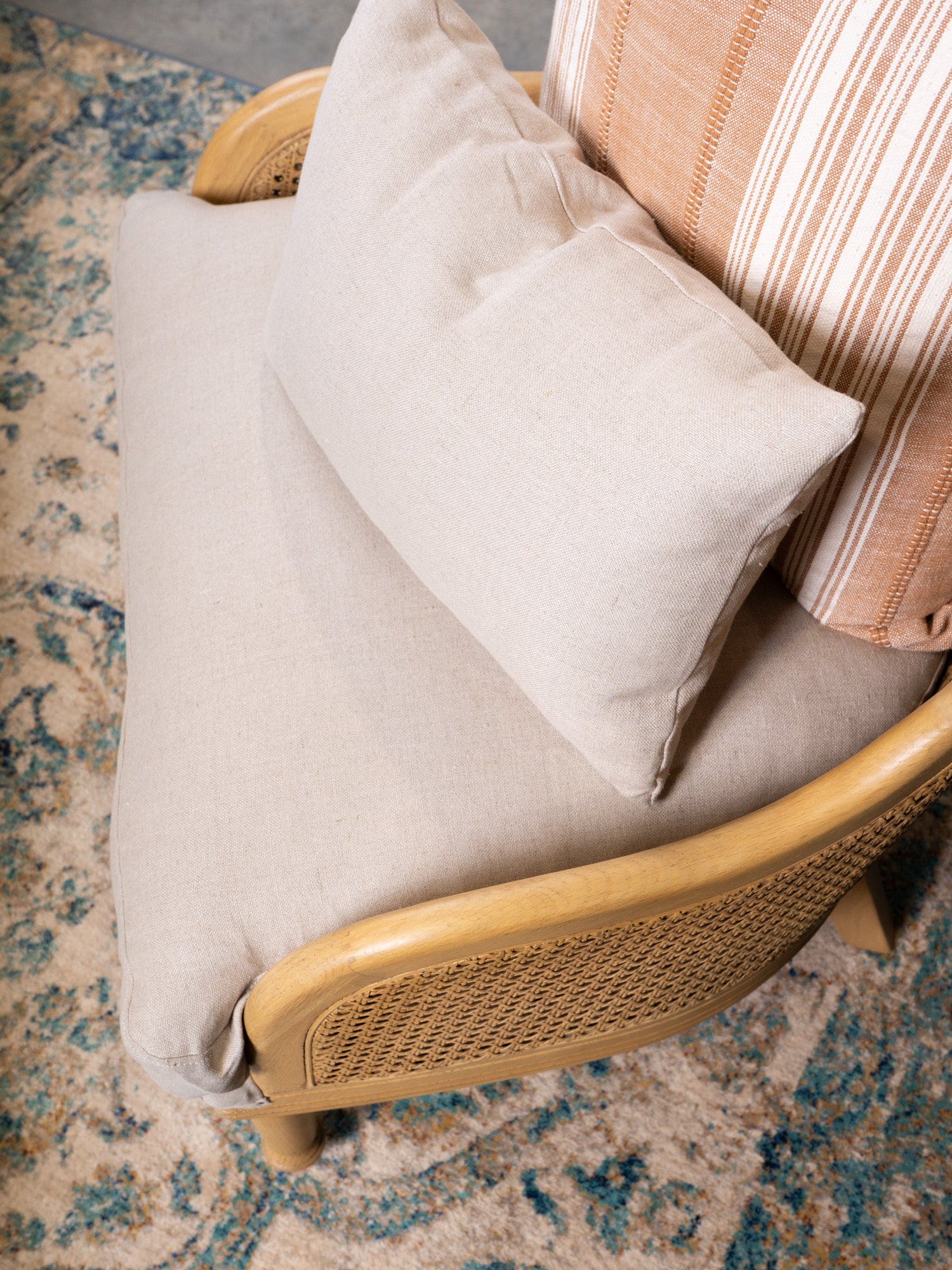 Wicker chair with beige cushion and striped pillow on a textured rug