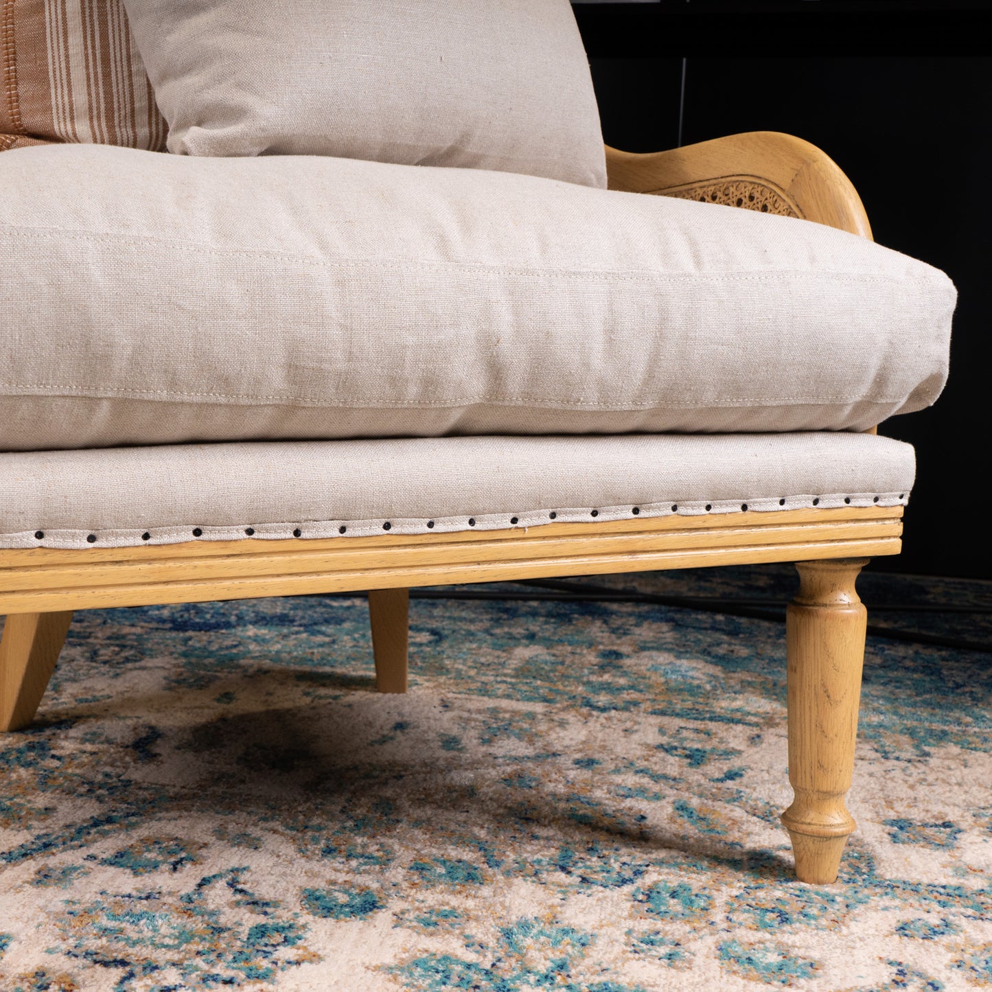 Close-up of a wooden chair with beige cushion on a patterned rug
