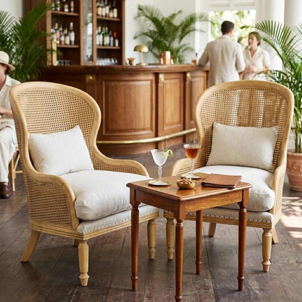 Two wicker chairs with white cushions and a small wooden table in a cozy room with people in the background.