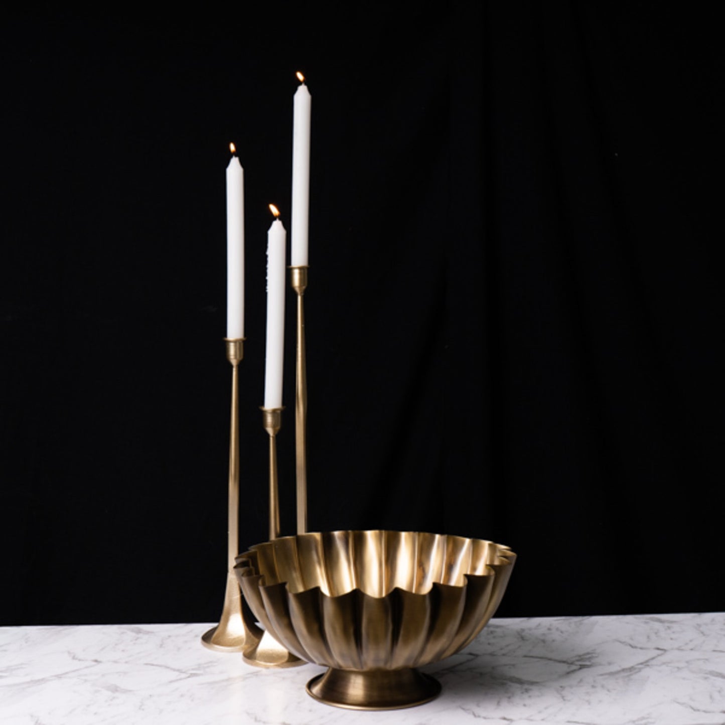Brass candle holder with three white candles on a dark background