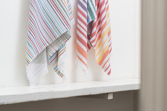 Colorful striped towels hanging on a white shelf.